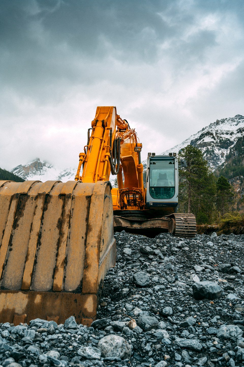 Excavator with bucket raised against a mountain sky, representative of heavy equipment consignments